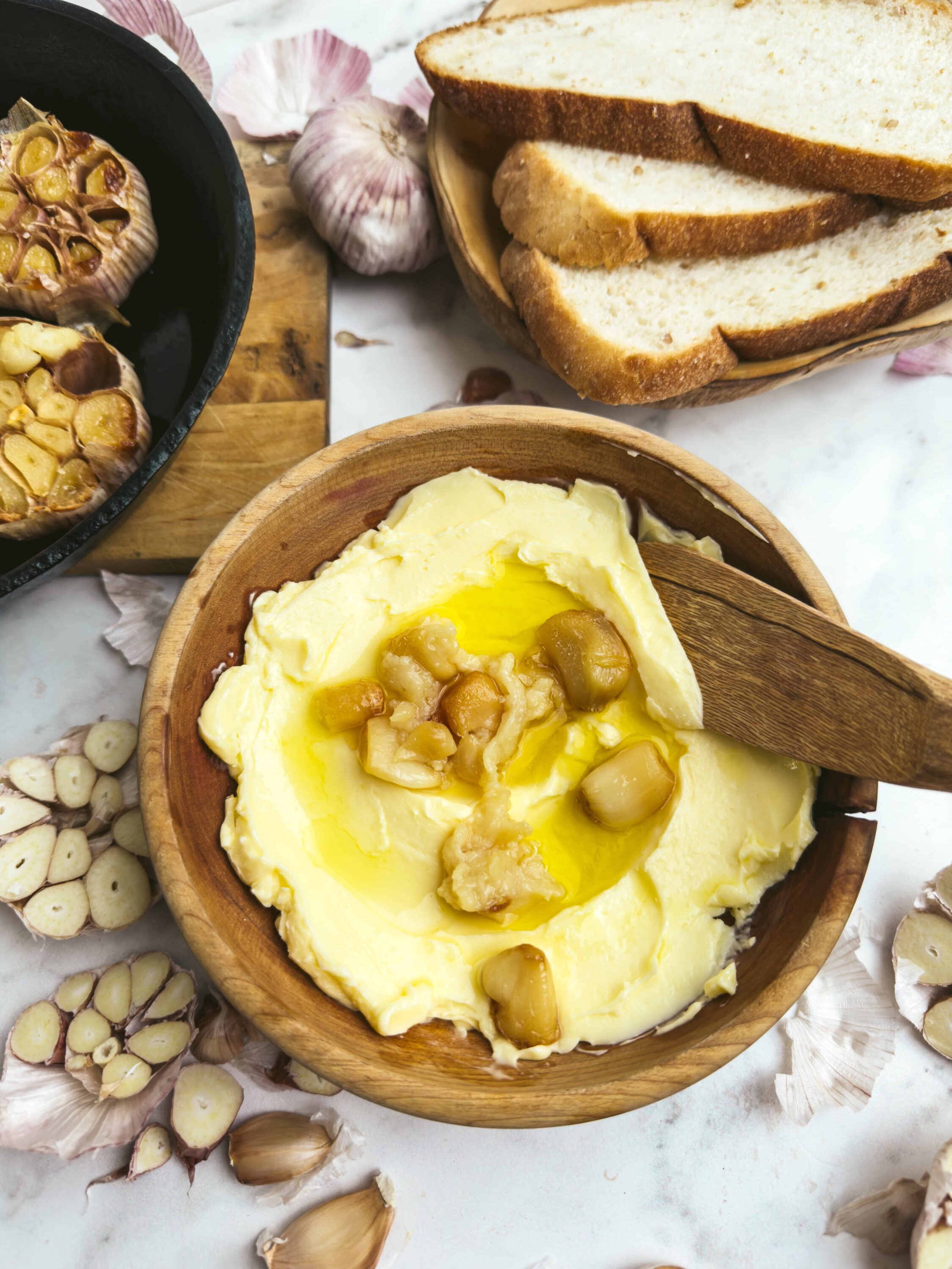 Creamy garlic butter mashed potatoes topped with roasted garlic cloves and olive oil, served in a rustic wooden bowl.