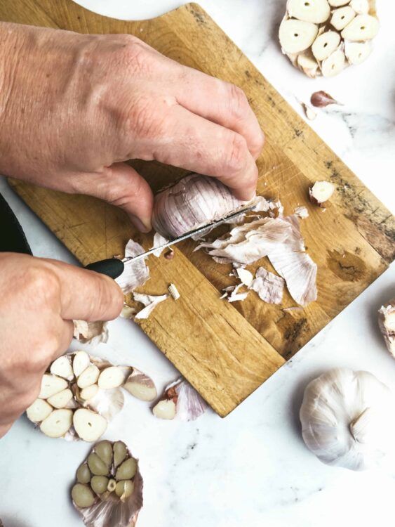 Fresh garlic being sliced on a wooden cutting board for cooking or baking.