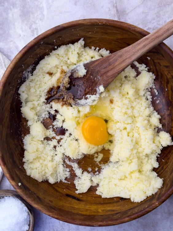 Butter, sugar, flour, egg, vanilla extract in wooden mixing bowl for baking recipe.