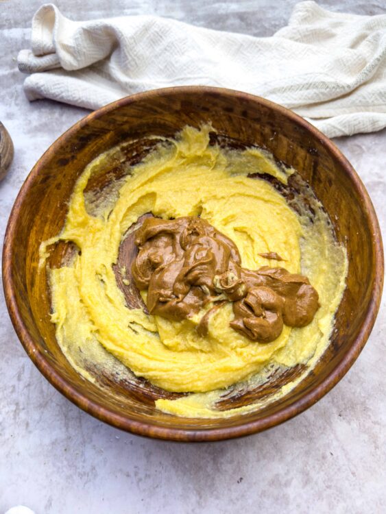 Creamy peanut butter stirred into fluffy mashed potatoes in a rustic wooden bowl for a delicious comfort food dish.