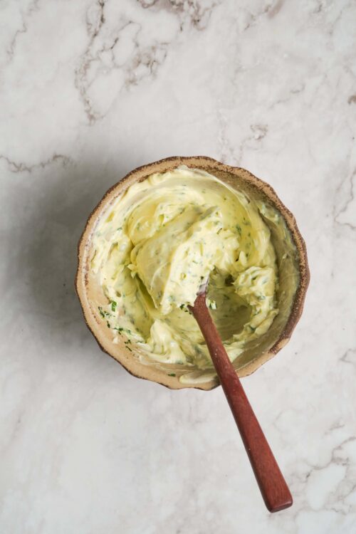 Creamy homemade herb butter in a rustic ceramic bowl on marble surface, ready for spreading or cooking.