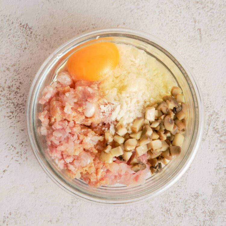 Minced chicken, mushroom, egg, and cheese mixture in a glass bowl for chicken mushroom casserole.
