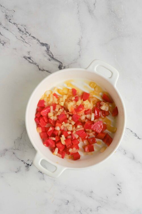 Diced vegetables in a white ceramic baking dish on marble countertop.