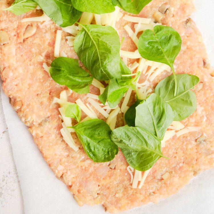 Cheese and basil topping pizza dough ready for baking.