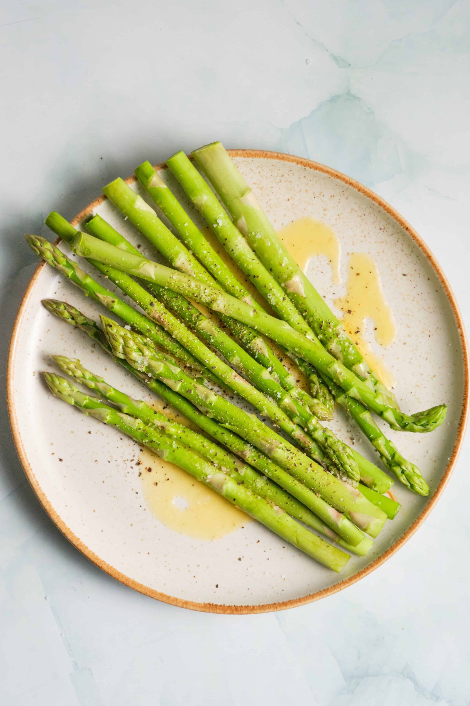 Fresh roasted asparagus spears drizzled with olive oil and sprinkled with black pepper served on a white ceramic plate.