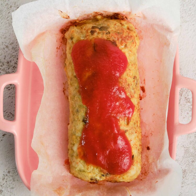 Baked vegetable loaf with tomato sauce on parchment paper in pink baking dish.