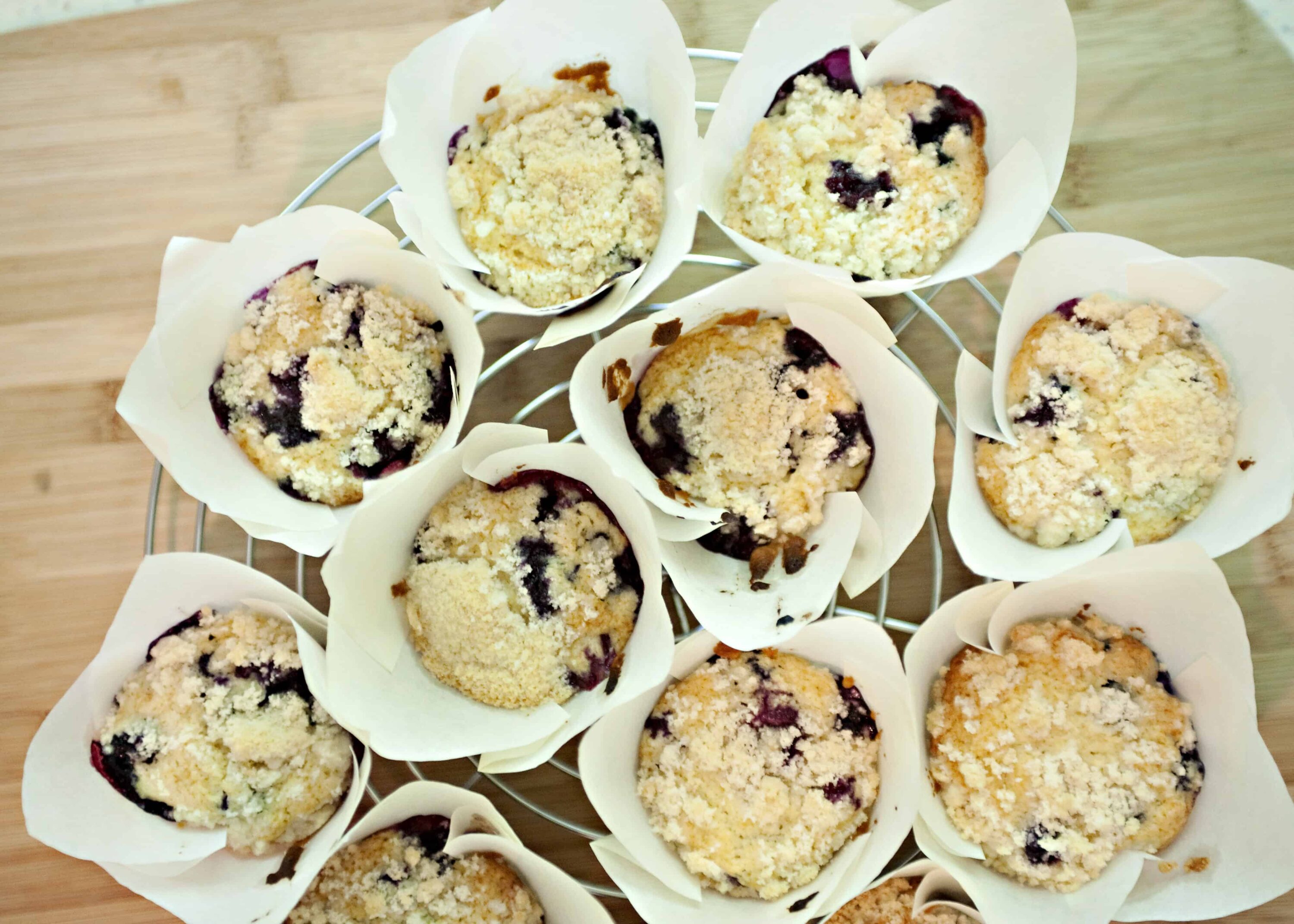 Freshly baked blueberry crumble muffins in paper liners on a cooling rack.