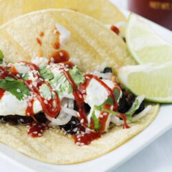 Tasty beef taco on a soft corn tortilla with cilantro, onions, and salsa, served with lime wedges on a white plate.