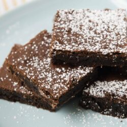Rich, fudgy chocolate brownies topped with powdered sugar on a light blue plate.
