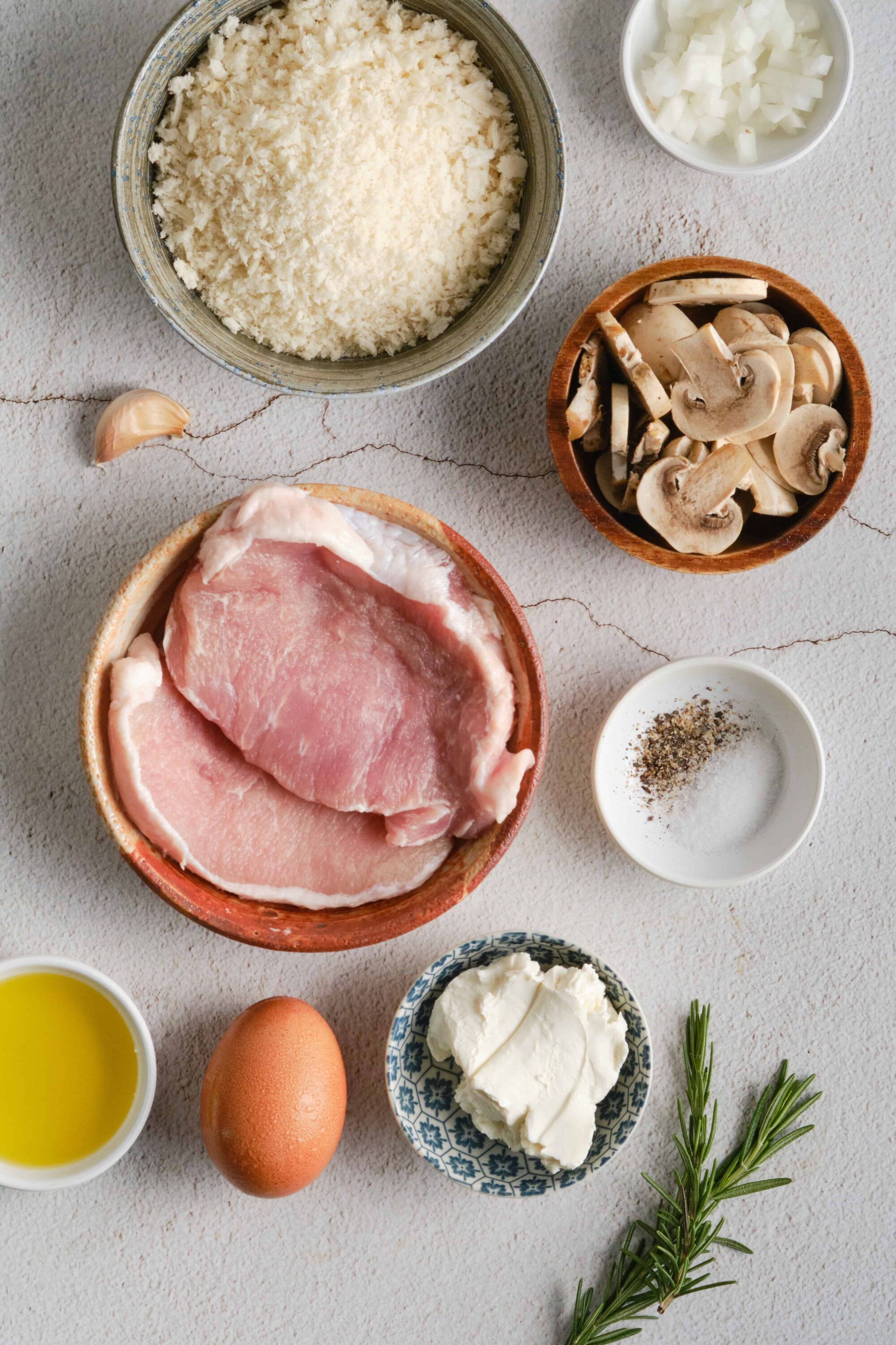 Minced chicken and mushroom ingredients for a baked dish, arranged on a textured white surface.