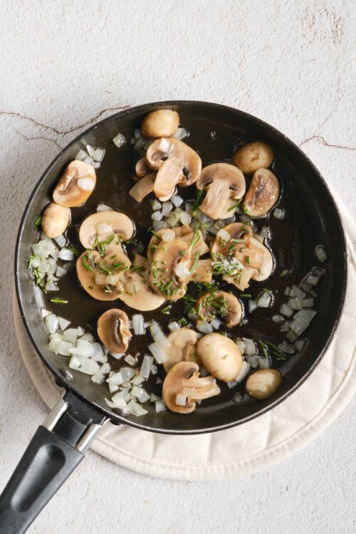 Sautéed mushrooms with chopped onions and fresh herbs in a black skillet.
