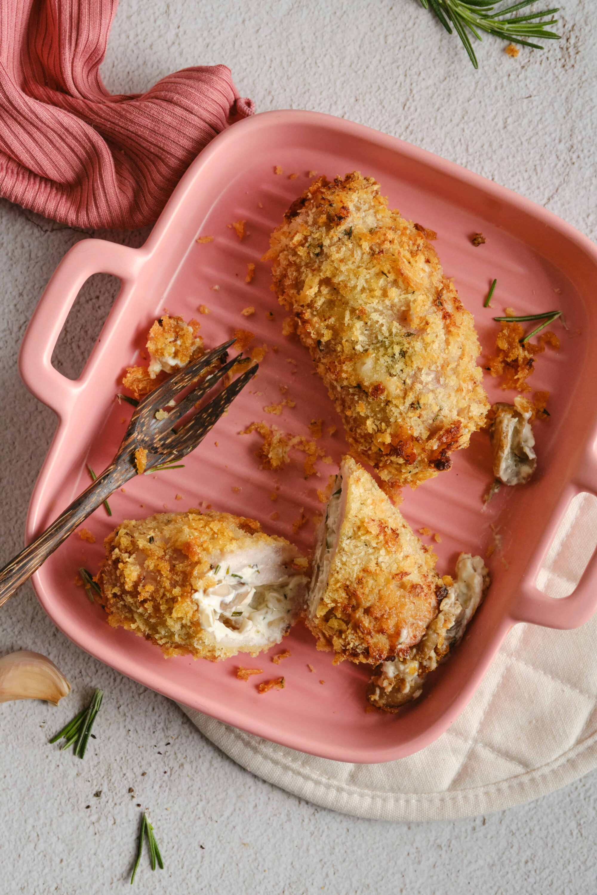 Breaded chicken cordon bleu on a pink baking dish, some with creamy stuffing. Perfect comfort food recipe from Baked Bree.