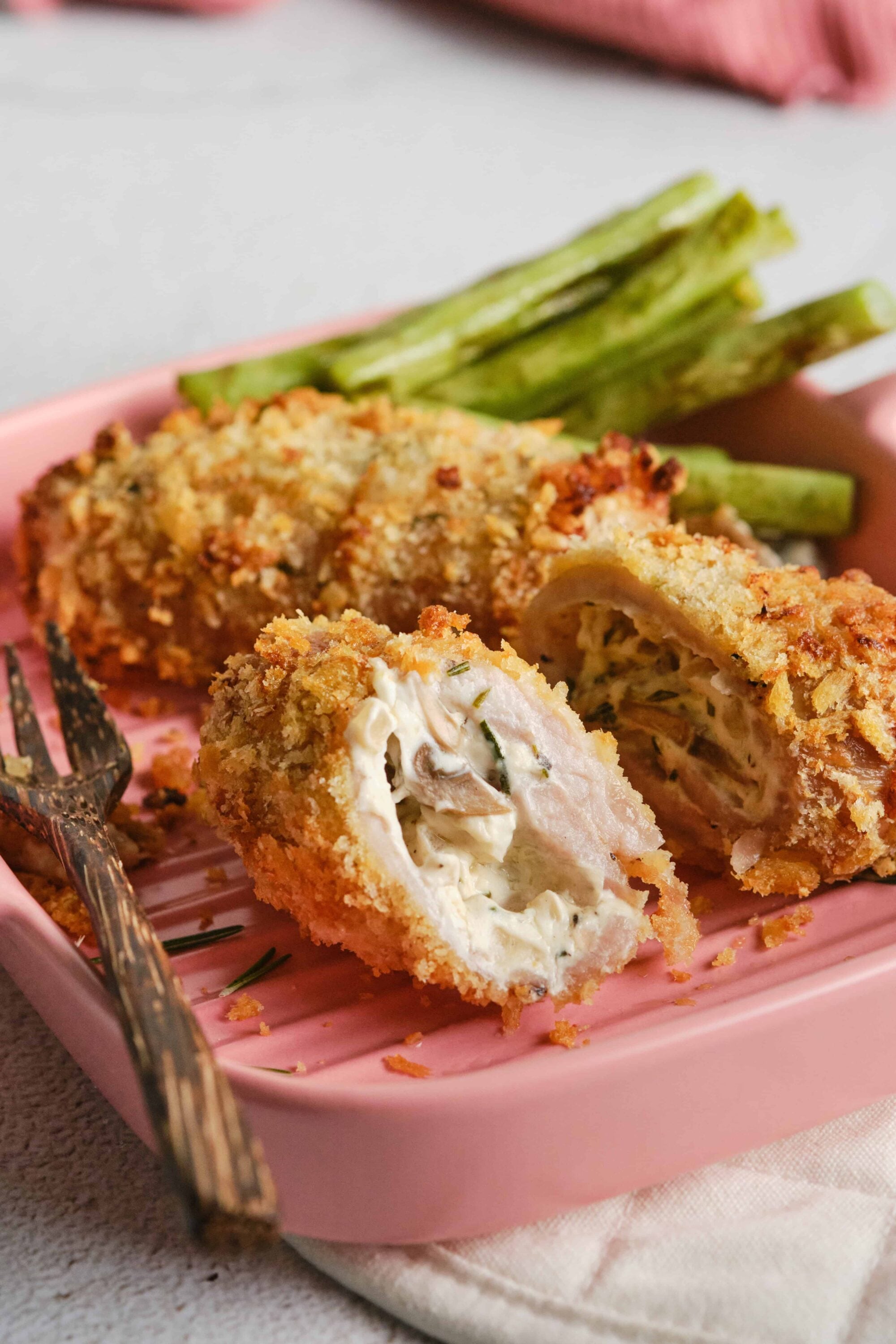 Crispy chicken cordon bleu with green beans on pink plate.