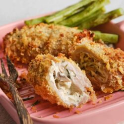 Crispy chicken cordon bleu with green beans on pink plate.