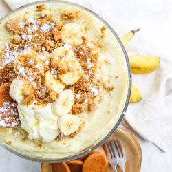 Banana pudding dessert with whipped cream and toasted cookie crumbs, served in a glass bowl.