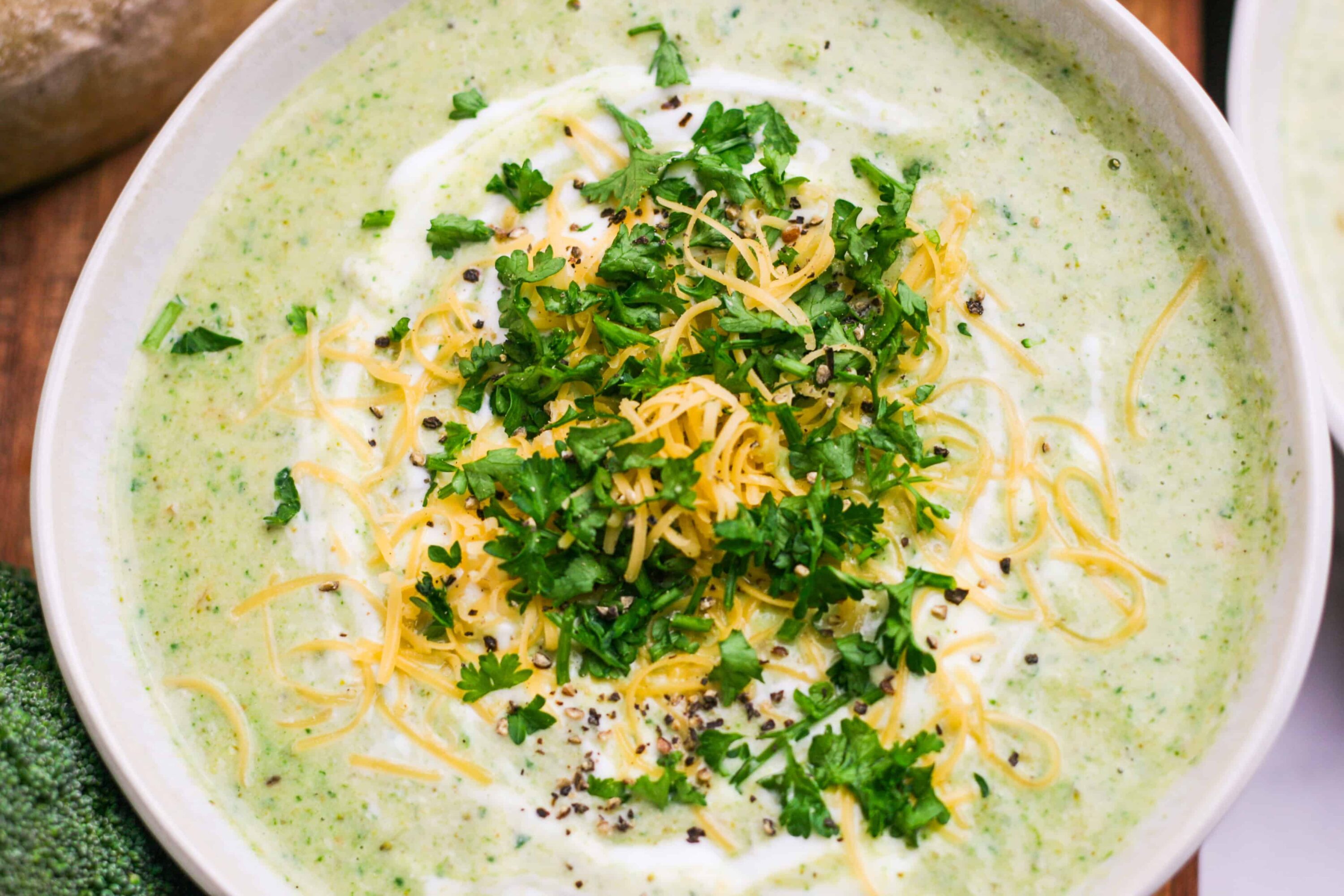 Creamy broccoli cheese soup with fresh herbs and shredded cheese on top.