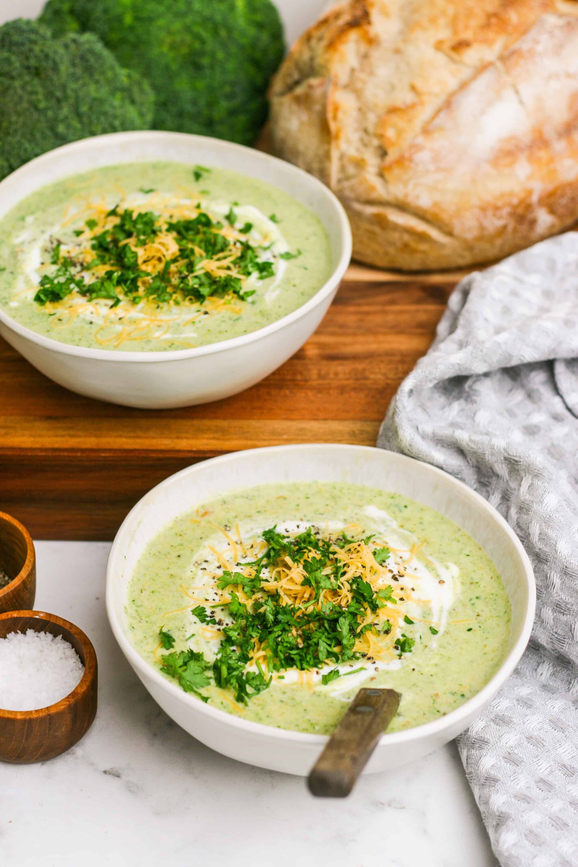 Creamy broccoli cheese soup with shredded cheese and fresh herbs in a white bowl.