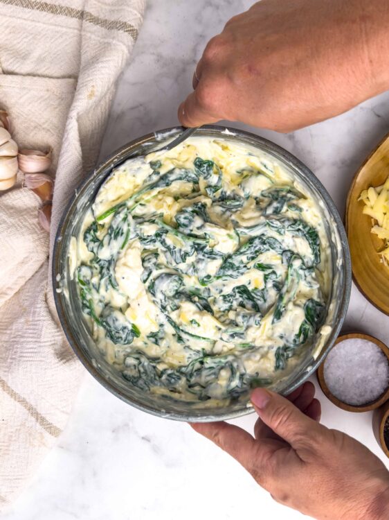 Creamy spinach and artichoke dip in a glass bowl, ready to serve or bake. Perfect for parties and gatherings.