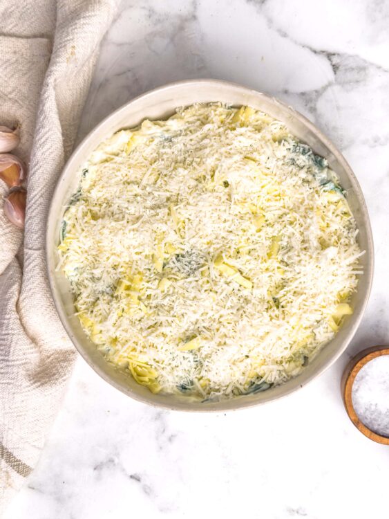 Creamy cheese layered casserole with shredded cheese and herbs, ready for baking.