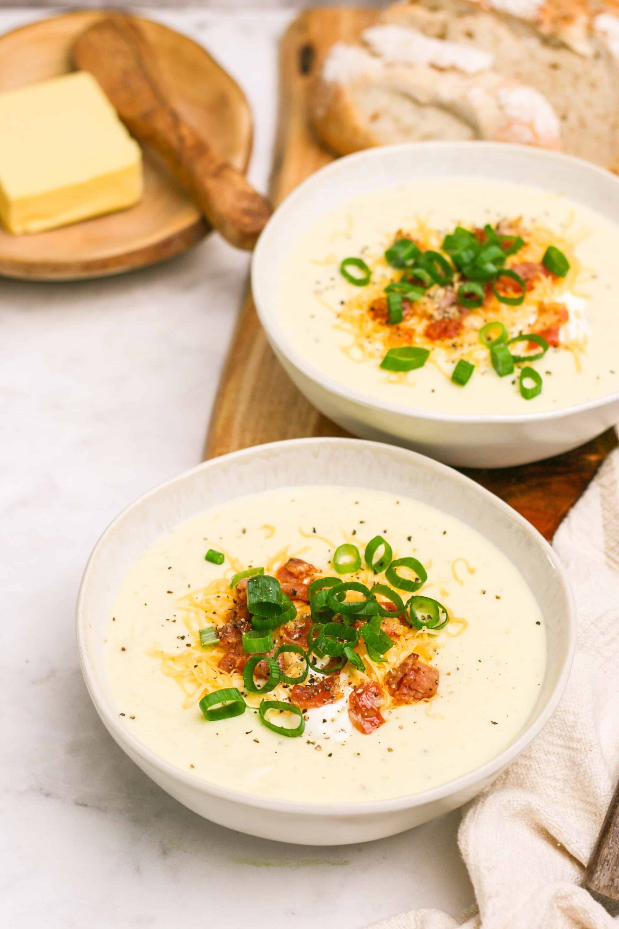 Creamy potato soup with shredded cheese, bacon, and green onions garnish. Perfect comfort food recipe from Baked Bree.