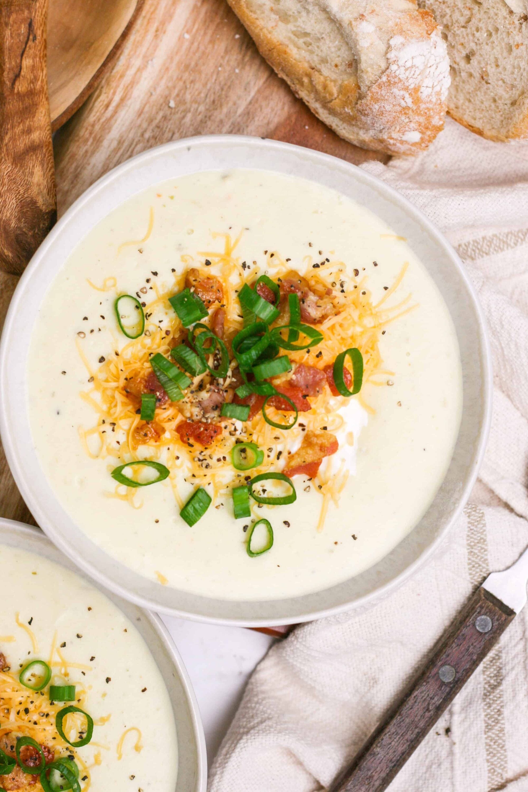 Creamy potato soup garnished with bacon, shredded cheddar, and green onions on a rustic table.