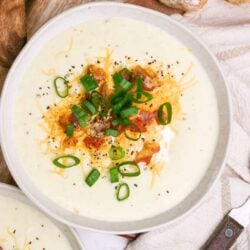 Creamy potato soup garnished with bacon, shredded cheddar, and green onions on a rustic table.
