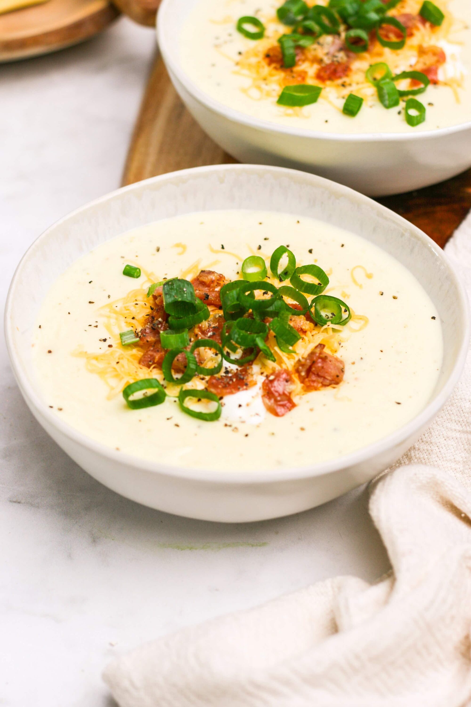 Savory creamy potato soup garnished with bacon and green onions in a white bowl.
