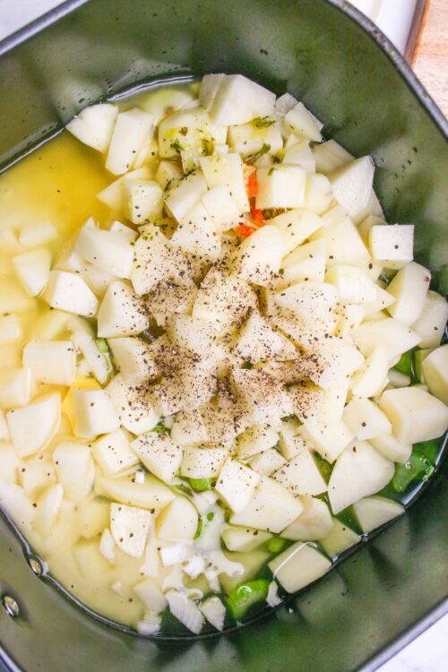 Diced potatoes, chopped onions, and seasonings in a cooking pot, ready for a savory recipe.
