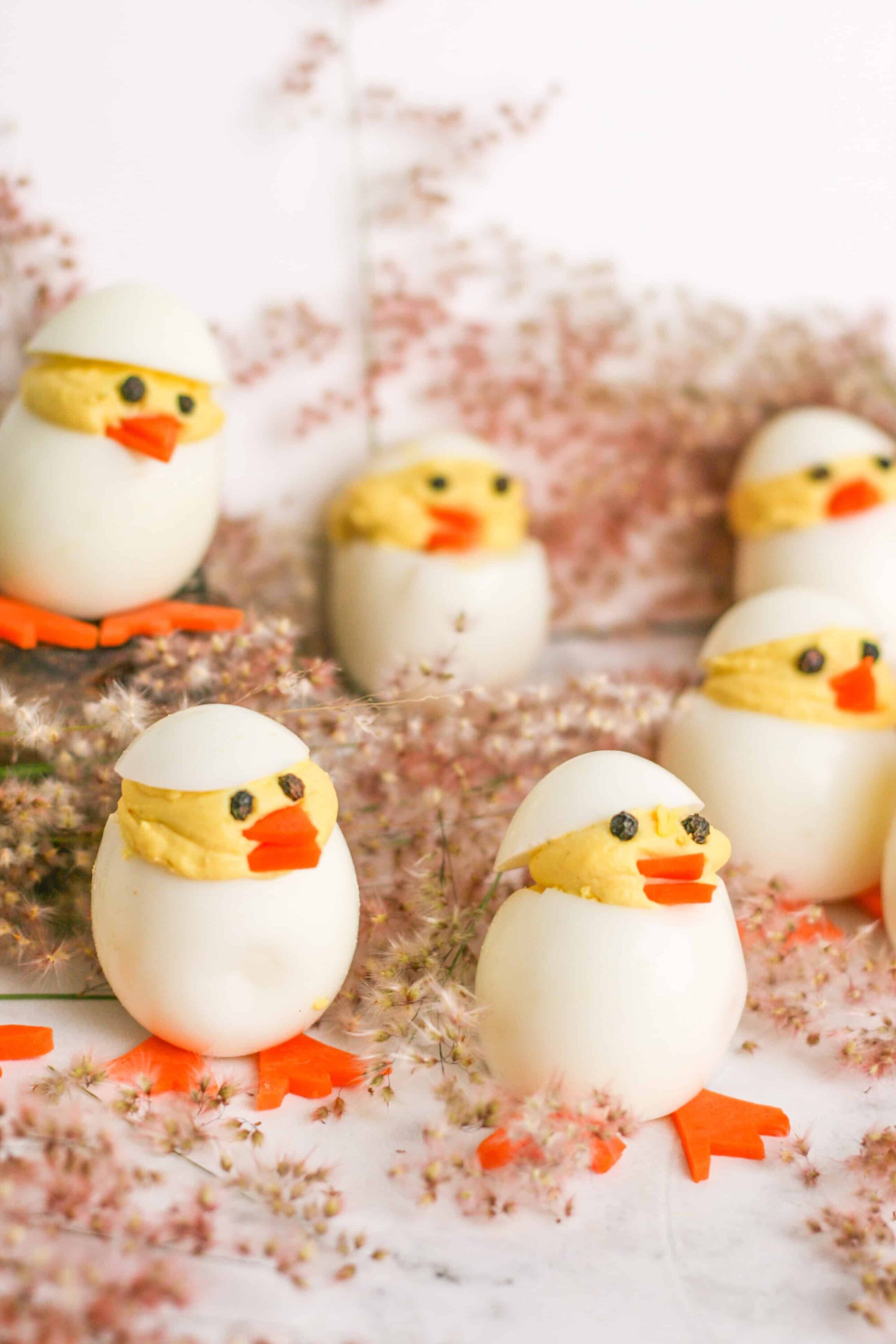 Cute Easter deviled eggs decorated as baby chicks with carrots, black peppercorn eyes, and egg white eggshells, perfect for spring celebrations.