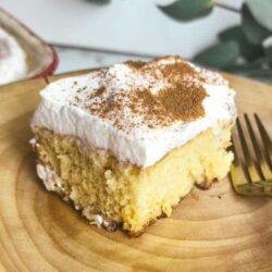 Creamy vanilla cake slice with whipped frosting and cinnamon powder, served on wooden platter.