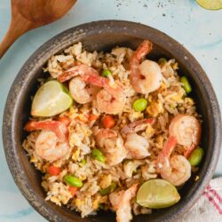Shrimp fried rice with lime wedges and vegetables in a rustic bowl, served as a flavorful Asian-inspired dish.