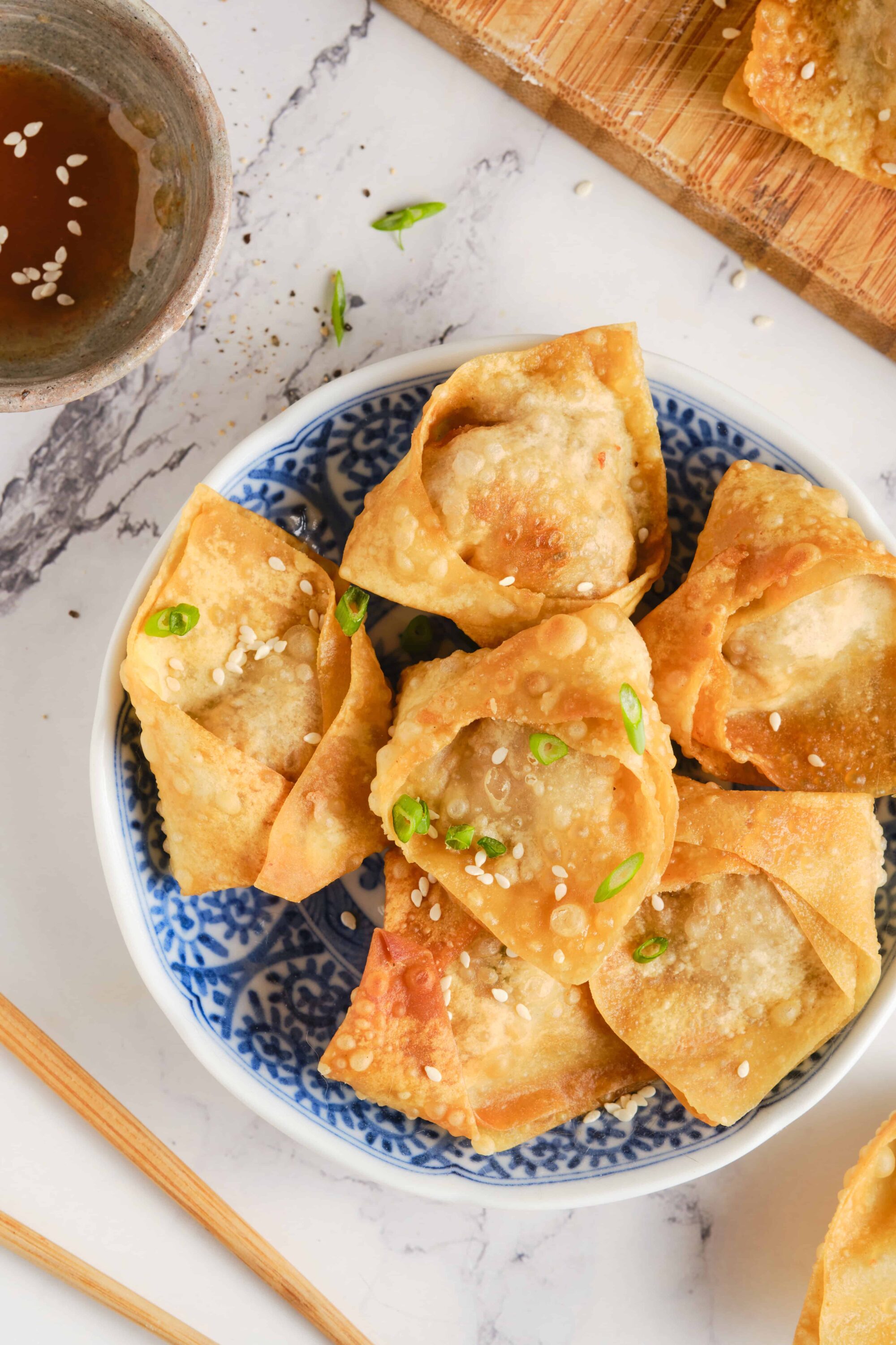 Crispy Asian potstickers with sesame seeds and chopped green onions, served on a decorative blue and white dish.