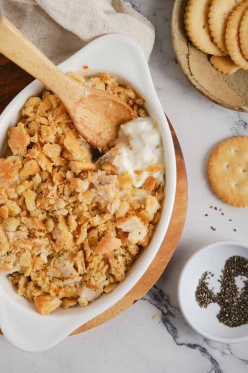 Crispy baked chicken casserole topped with golden cracker crumble and creamy mashed potatoes in a white baking dish.