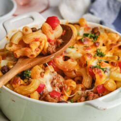 Cheesy baked pasta with ground beef and vegetables in a white casserole dish.