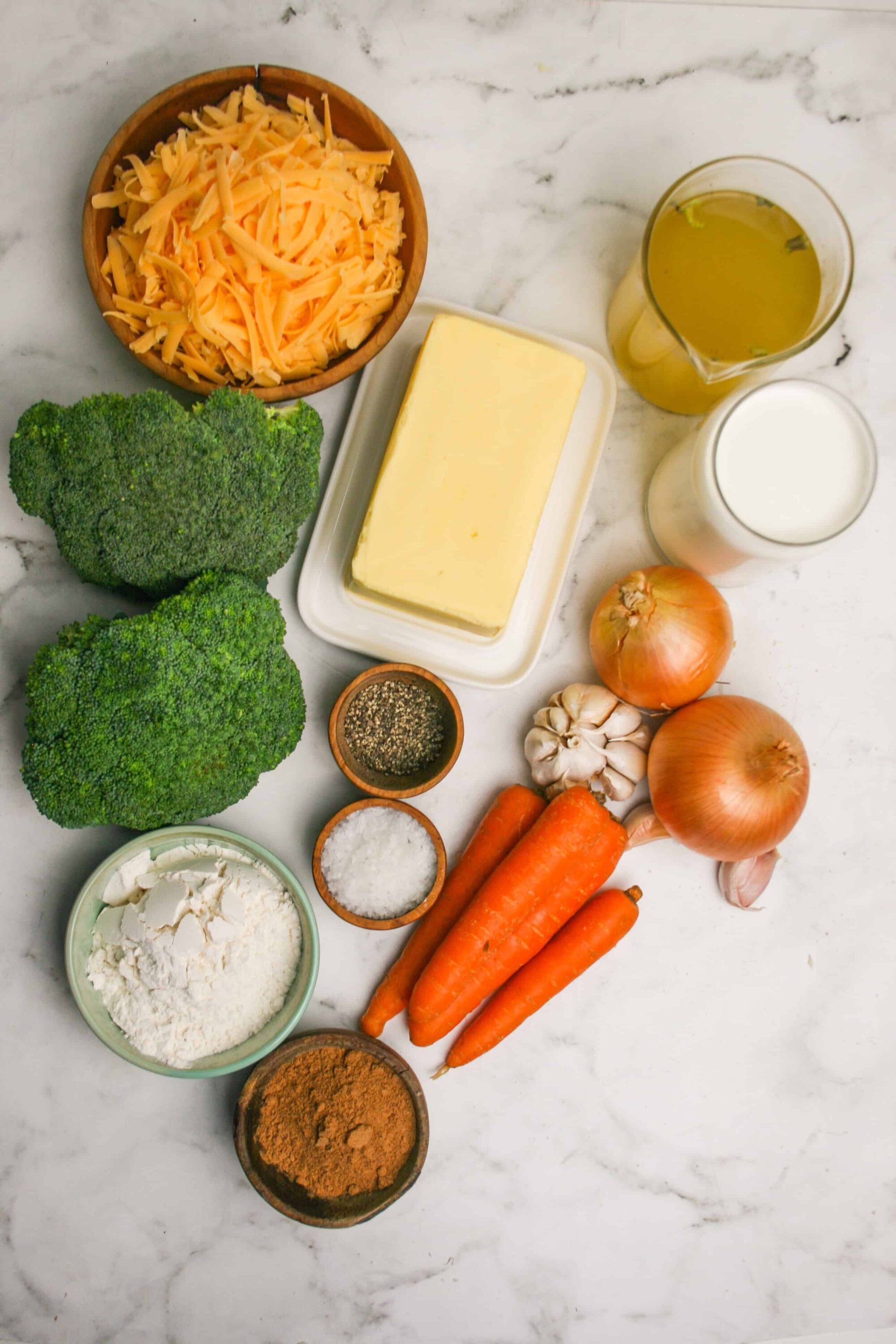 Shredded cheddar cheese, broccoli, carrots, onions, garlic, butter, milk, flour, spices, and seasonings for baked cheese broccoli recipe.