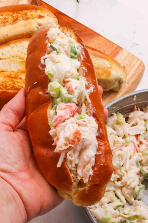 Creamy crab salad stuffed hot dog bun on wooden cutting board with toasted bread.
