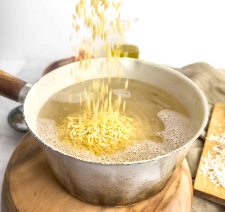 Golden orzo pasta cooking in a saucepan with water, ready for use in a delicious homemade recipe.