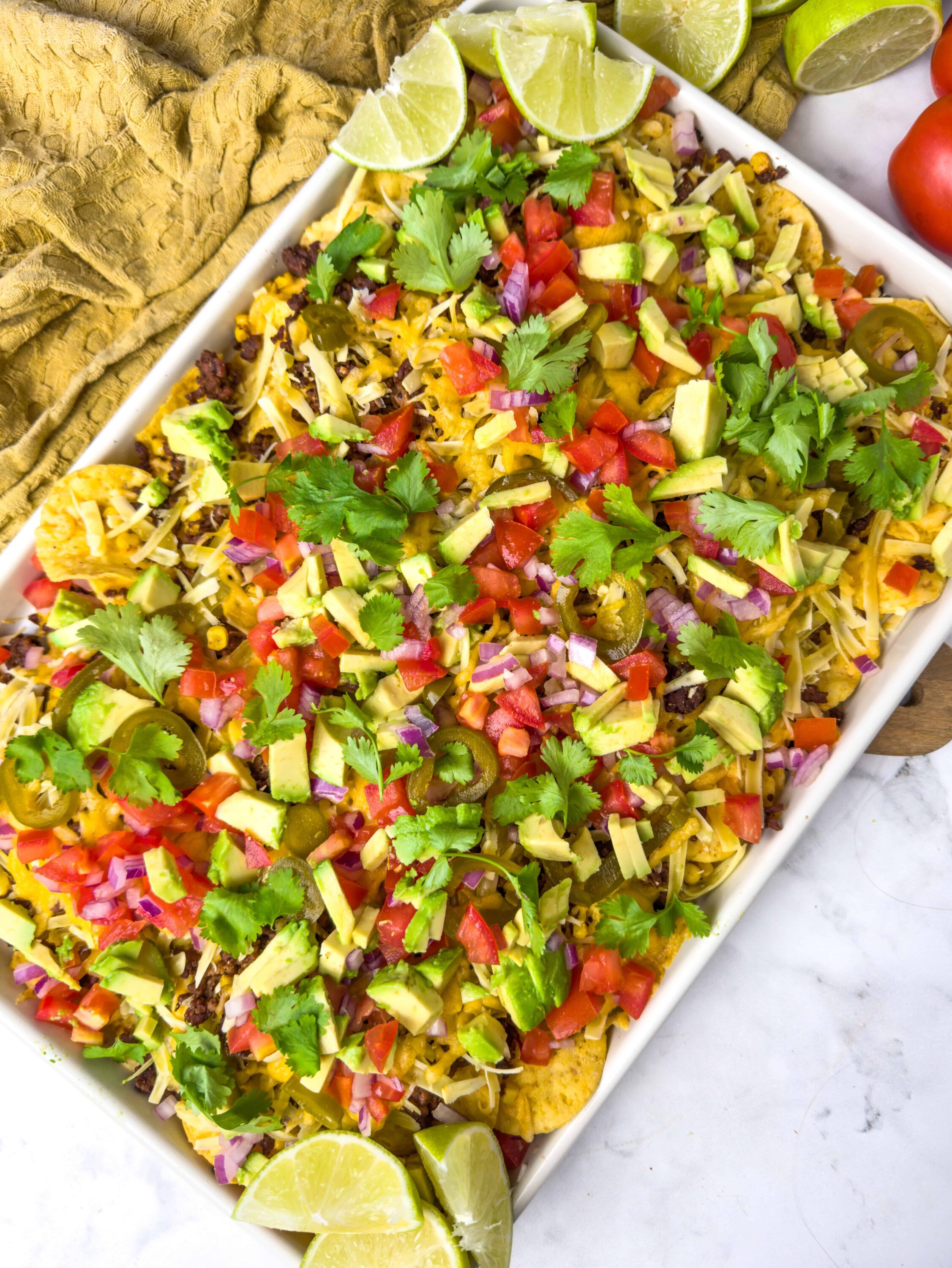Fresh homemade nachos topped with cheese, tomatoes, avocado, cilantro, and lime wedges. Perfect for game day or a snack.