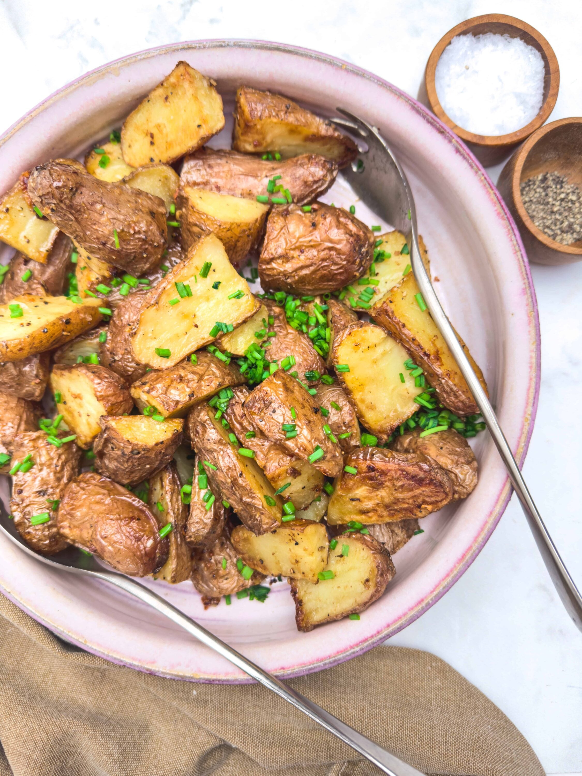 Golden roasted potatoes with chives, seasoned with salt and pepper, served in a pink-rimmed bowl.