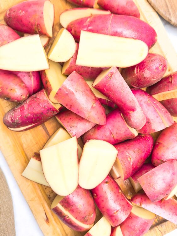 Fresh chopped red skinned potatoes on a wooden cutting board for roasting or boiling.
