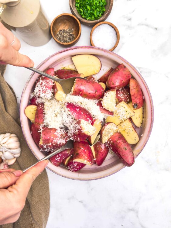 Sweet potato wedges in a bowl with grated cheese, garlic, and herbs, ready for baking or roasting.