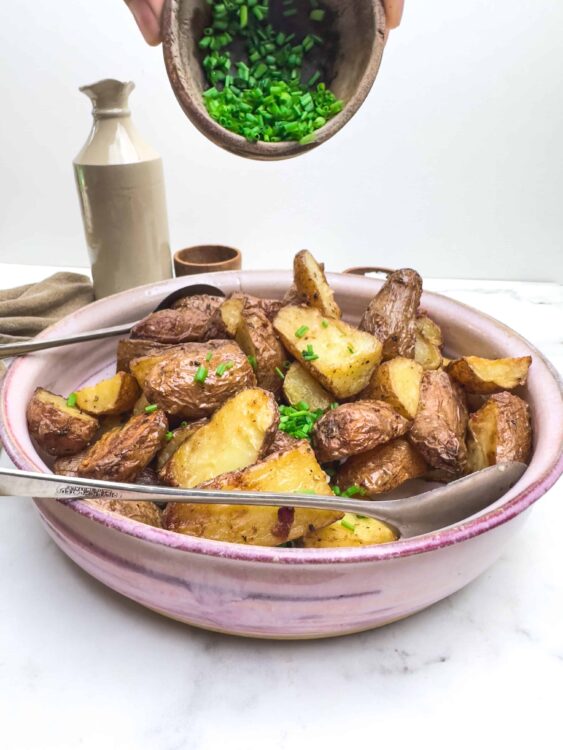 Crispy roasted potatoes garnished with chopped chives on a pink ceramic bowl.