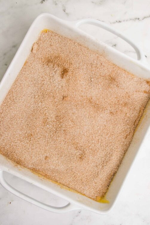 Cinnamon sugar coating on a dessert layer in a white baking dish.