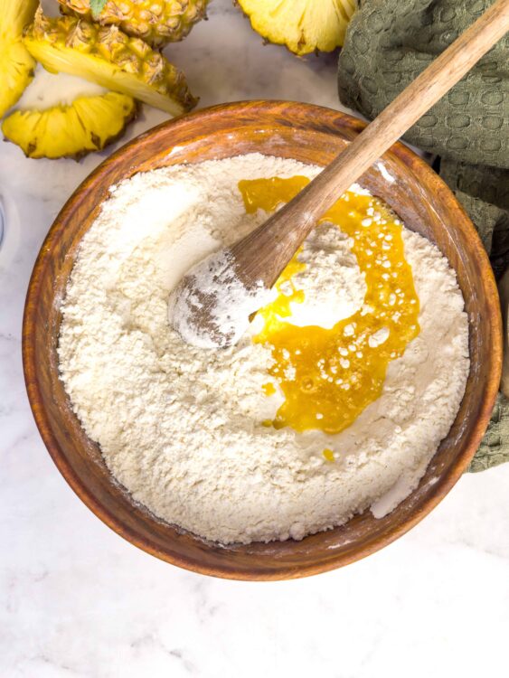 Flour, pineapple, and egg mixture in a wooden bowl for baking tropical pineapple cake.