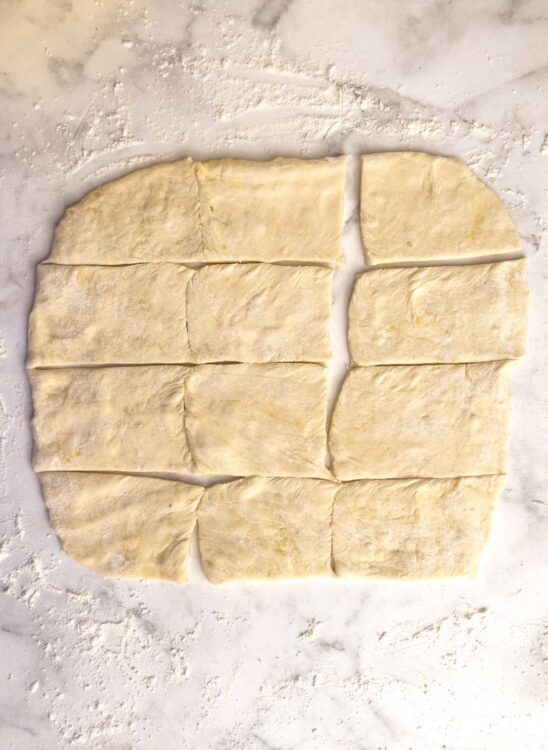 Buttery puff pastry dough for baking, cut into squares on floured surface.