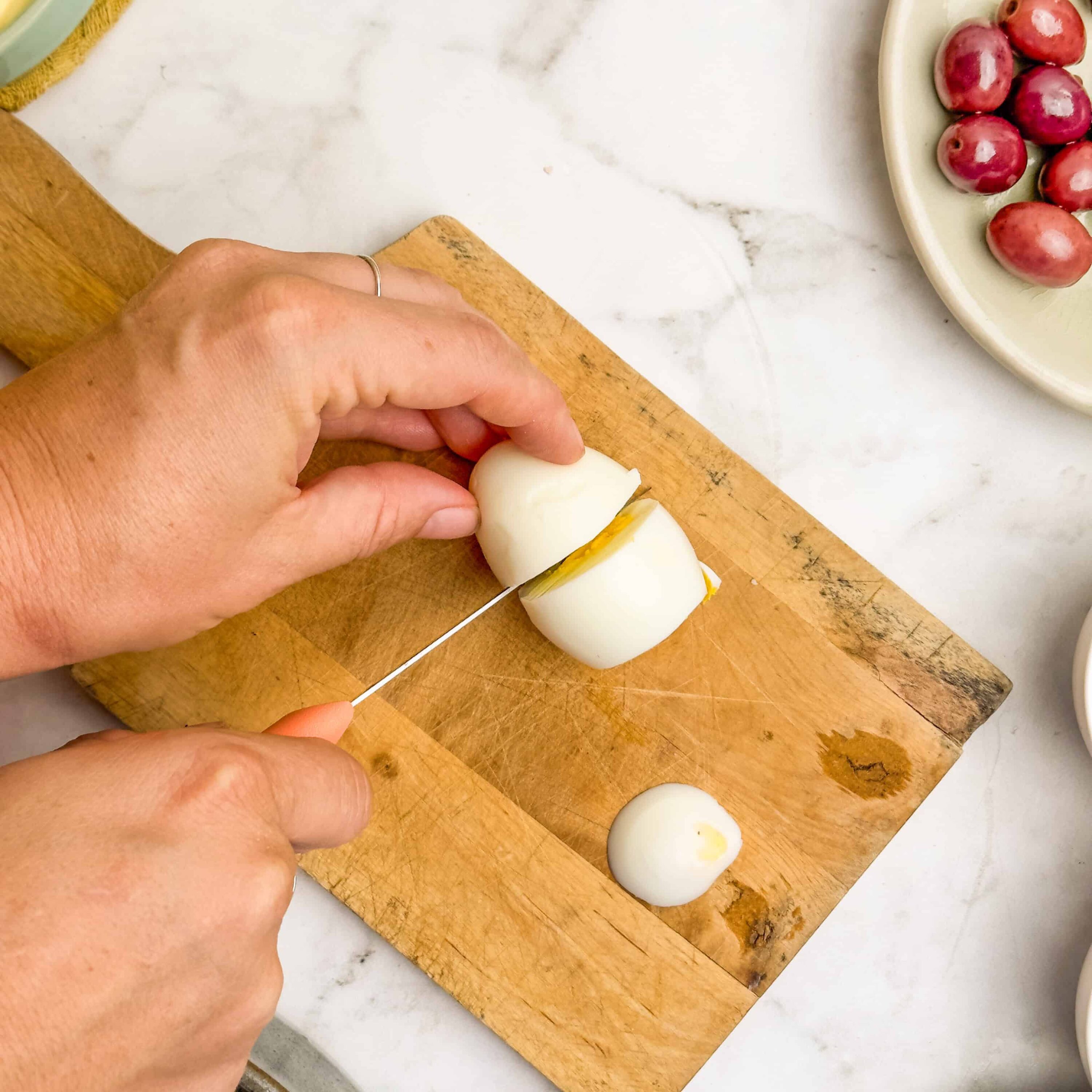Boiled egg being sliced on wooden cutting board in kitchen.