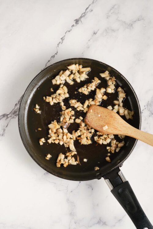 Minced garlic sautéing in a black frying pan on a white marble surface.