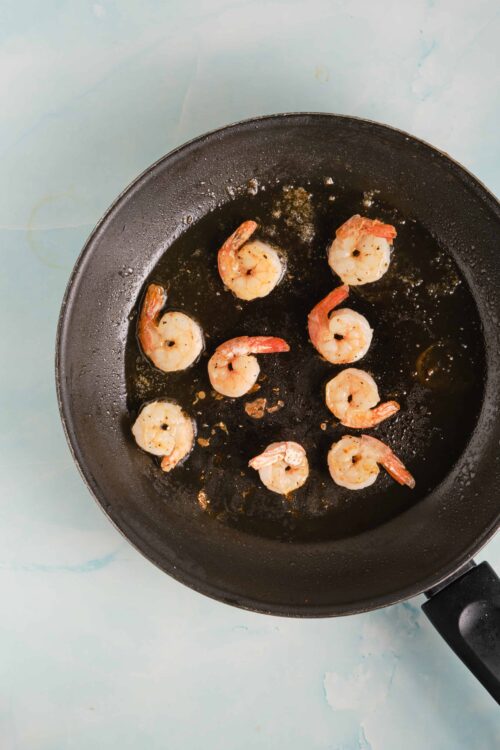 Juicy shrimp being sautéed in a black skillet, perfect for seafood recipes or appetizer dishes.