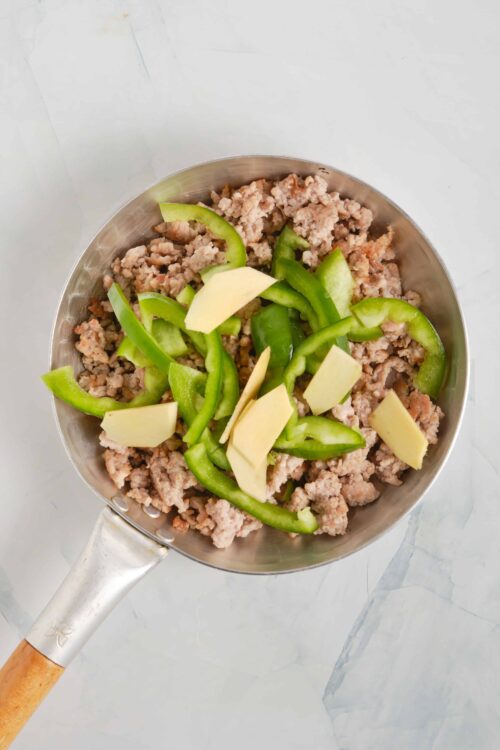 Minced meat with chopped green bell peppers and sliced ginger in a stainless steel pan.