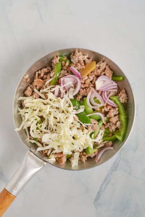 Minced pork with green bell peppers, onions, and shredded cabbage in a stainless steel pan.